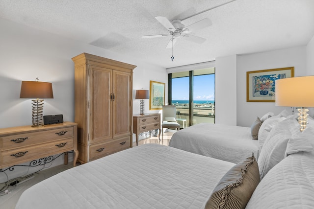 bedroom featuring ceiling fan, a water view, access to exterior, and a textured ceiling