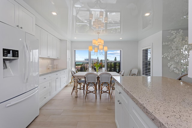 kitchen featuring white fridge with ice dispenser, light stone countertops, decorative light fixtures, an inviting chandelier, and white cabinets