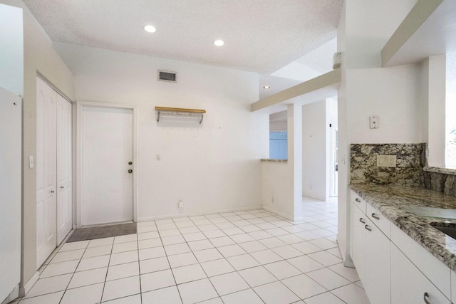 kitchen featuring tasteful backsplash, white cabinetry, light stone counters, and light tile patterned floors