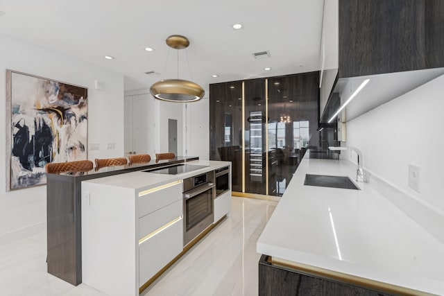 kitchen featuring black electric cooktop, oven, sink, a kitchen island, and hanging light fixtures