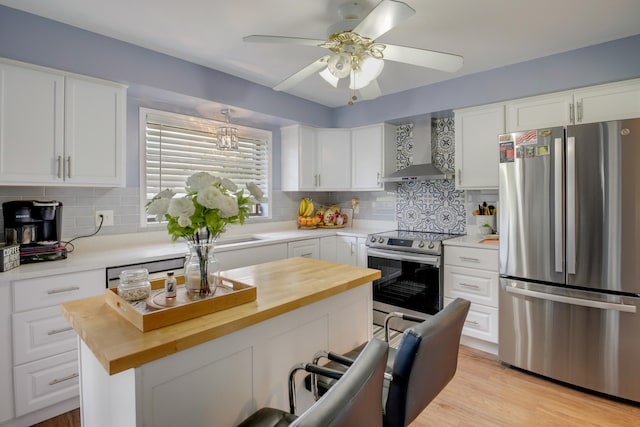 kitchen with white cabinetry, wooden counters, a center island, stainless steel appliances, and wall chimney exhaust hood