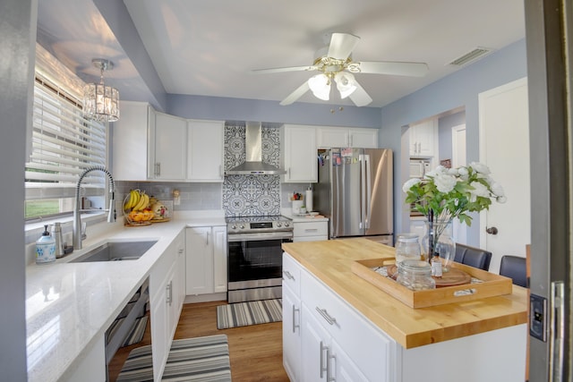 kitchen with hanging light fixtures, sink, wall chimney range hood, white cabinetry, and appliances with stainless steel finishes