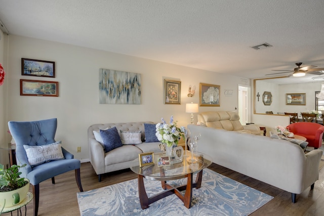 living room with ceiling fan, a textured ceiling, and dark wood-type flooring