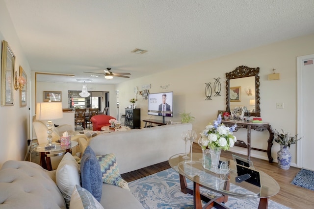 living room featuring wood-type flooring, a textured ceiling, and ceiling fan