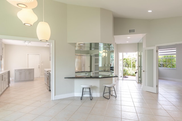 kitchen featuring high vaulted ceiling, light tile floors, decorative light fixtures, a breakfast bar area, and white cabinets