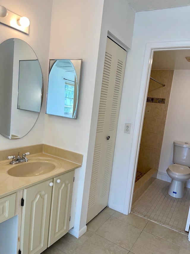 bathroom with tile patterned flooring, tiled shower, vanity, and toilet