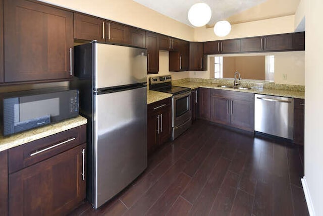 kitchen with dark brown cabinetry, light stone countertops, sink, stainless steel appliances, and dark hardwood / wood-style floors