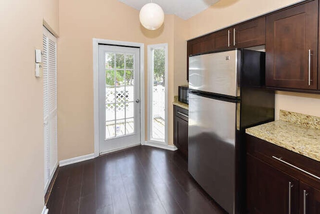 kitchen featuring hanging light fixtures, stainless steel fridge, light stone countertops, dark brown cabinets, and dark hardwood / wood-style flooring