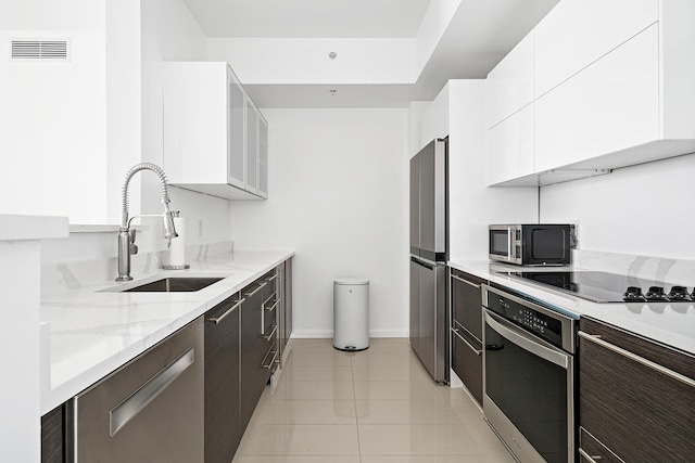 kitchen with sink, white cabinets, stainless steel appliances, light tile patterned floors, and dark brown cabinetry