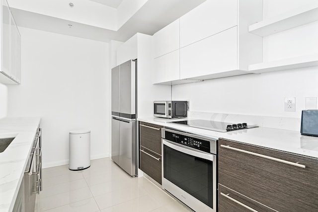 kitchen with appliances with stainless steel finishes, light tile patterned flooring, white cabinetry, light stone counters, and dark brown cabinetry