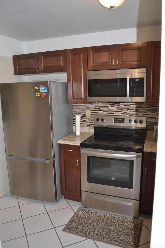 kitchen with light tile floors, appliances with stainless steel finishes, tasteful backsplash, and light stone counters