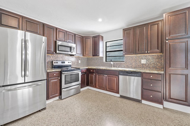 kitchen featuring sink, stainless steel appliances, light stone counters, dark brown cabinets, and tasteful backsplash