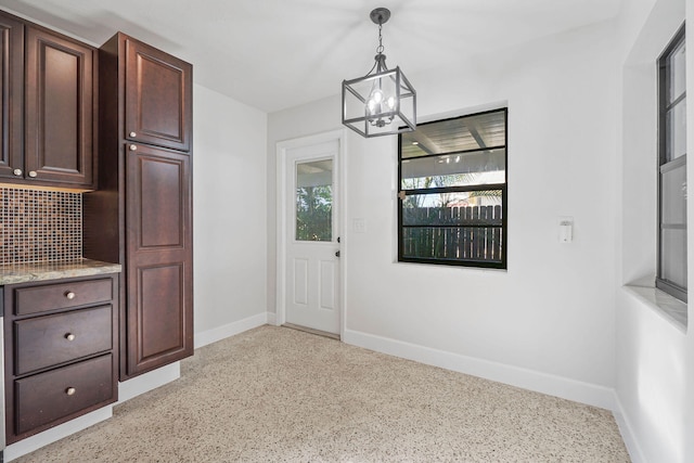 interior space with pendant lighting, tasteful backsplash, a notable chandelier, dark brown cabinetry, and light stone countertops