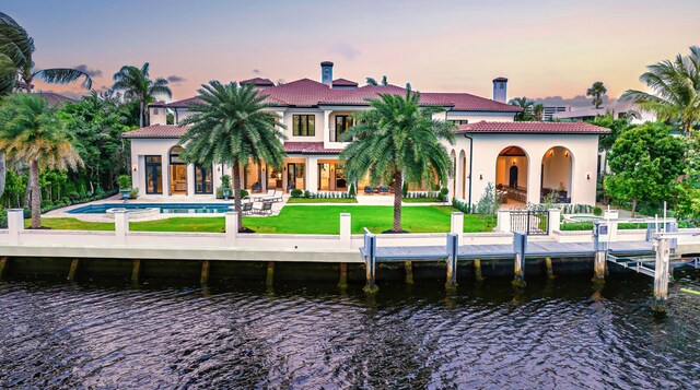 back house at dusk featuring a water view, a yard, a patio, and a balcony