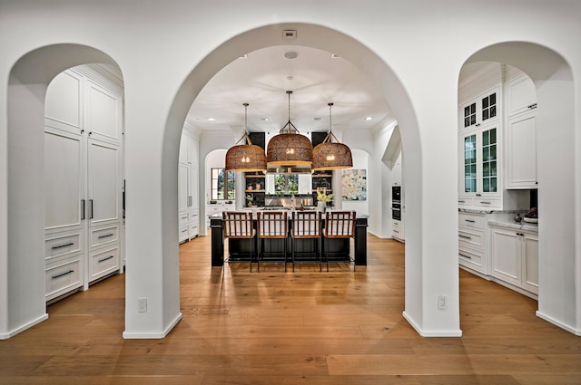 kitchen featuring a center island, hanging light fixtures, light hardwood / wood-style floors, white cabinetry, and a breakfast bar area