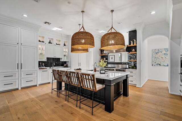 kitchen with backsplash, a kitchen island with sink, crown molding, decorative light fixtures, and white cabinets