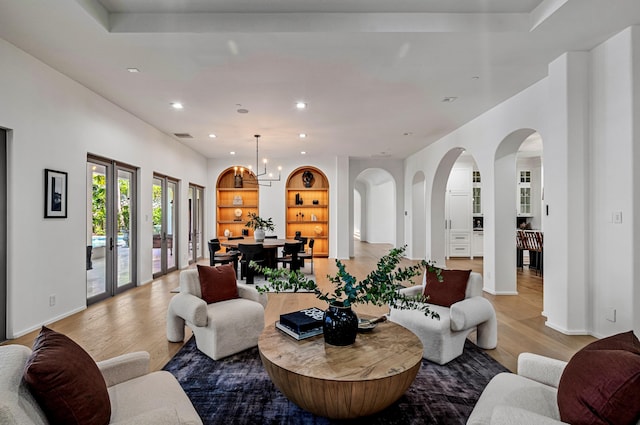 living room featuring french doors, light hardwood / wood-style floors, built in features, and a notable chandelier