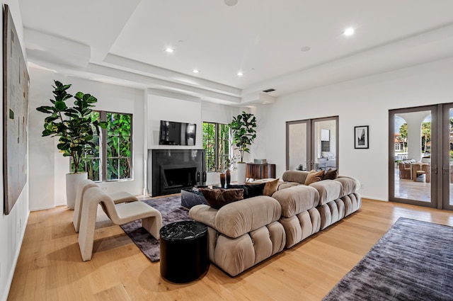 living room with a wealth of natural light, a raised ceiling, a high end fireplace, and light hardwood / wood-style flooring