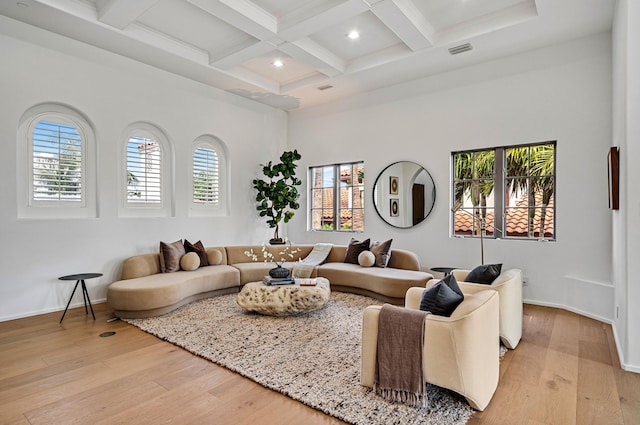 living room featuring a towering ceiling, beamed ceiling, light hardwood / wood-style floors, and coffered ceiling