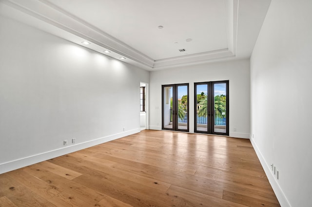 empty room with french doors, a tray ceiling, and light hardwood / wood-style flooring