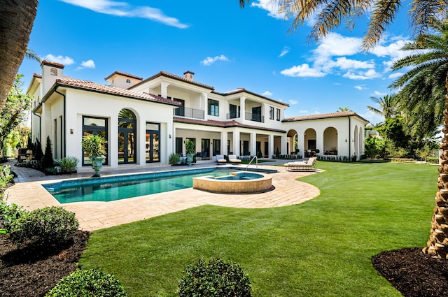 rear view of property featuring a pool with hot tub, a balcony, a patio, and a lawn