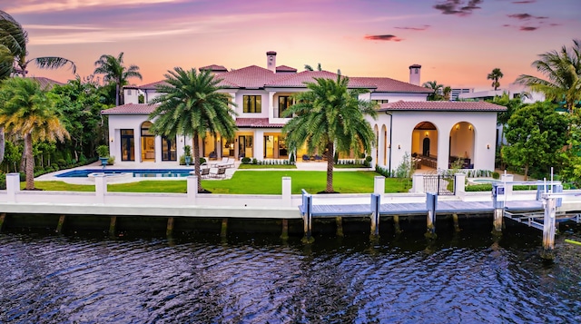 back house at dusk featuring a lawn, a water view, and a patio