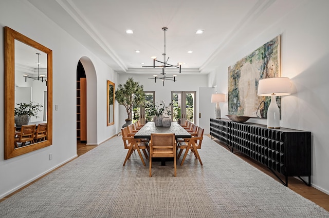 dining space featuring an inviting chandelier, a raised ceiling, wood-type flooring, and french doors