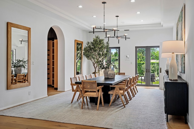 dining space featuring french doors, light hardwood / wood-style flooring, a raised ceiling, and a notable chandelier