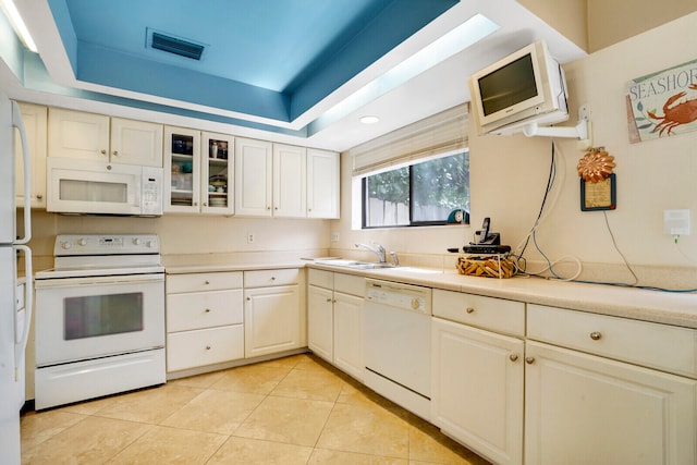 kitchen featuring white appliances, a tray ceiling, sink, and light tile floors