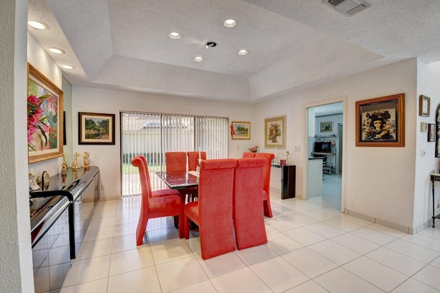 dining space with light tile patterned floors, a textured ceiling, and a raised ceiling