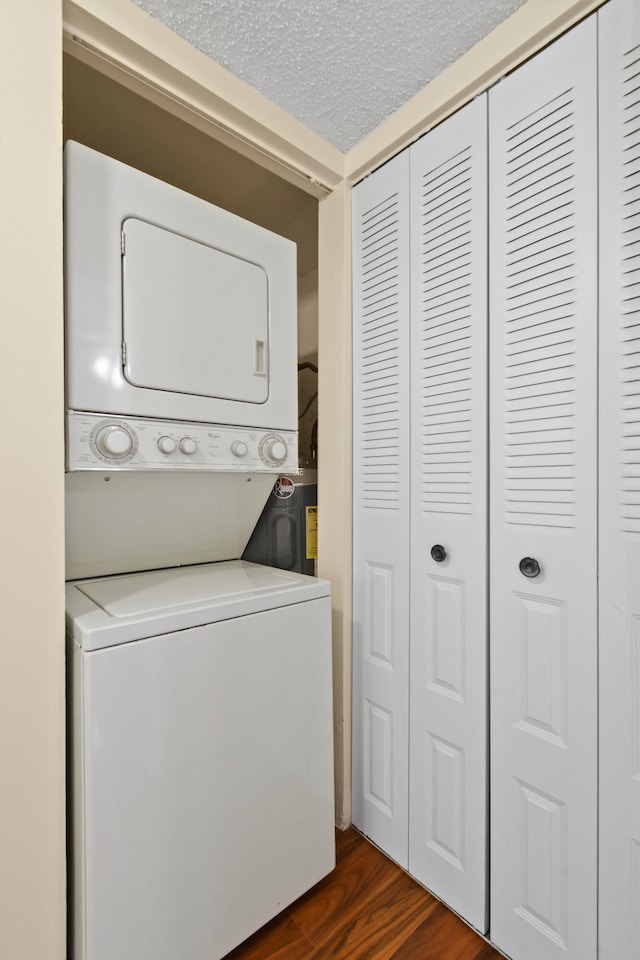 clothes washing area featuring stacked washer / drying machine, dark hardwood / wood-style floors, and a textured ceiling