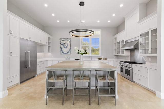 kitchen with a center island, white cabinets, range hood, premium appliances, and a breakfast bar area