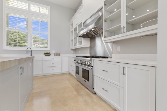 kitchen with white cabinets, wall chimney exhaust hood, and range with two ovens