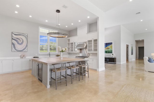 kitchen with white cabinetry, a center island, wall chimney range hood, wood counters, and a kitchen breakfast bar