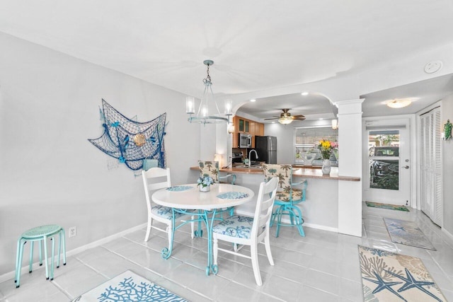 dining room featuring decorative columns, sink, ceiling fan with notable chandelier, and light tile patterned floors