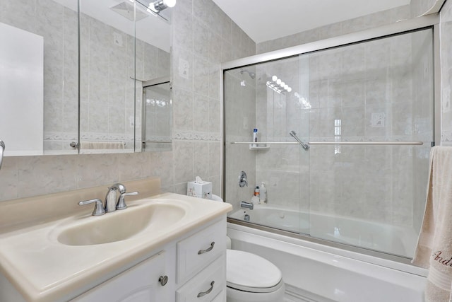 full bathroom with tile walls, toilet, vanity with extensive cabinet space, and bath / shower combo with glass door