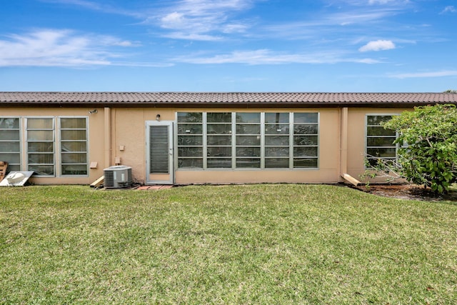 rear view of property with central AC unit and a lawn