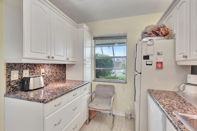 kitchen with backsplash, white appliances, dark stone countertops, white cabinets, and light tile floors