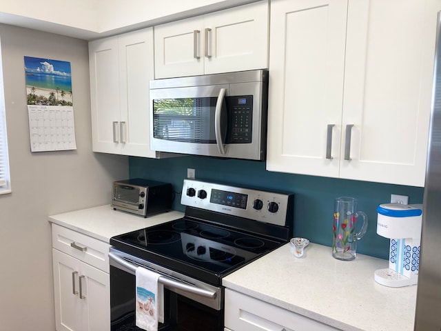 kitchen featuring stainless steel appliances, light stone countertops, and white cabinetry