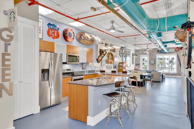 kitchen featuring sink, ceiling fan, appliances with stainless steel finishes, concrete floors, and a breakfast bar area