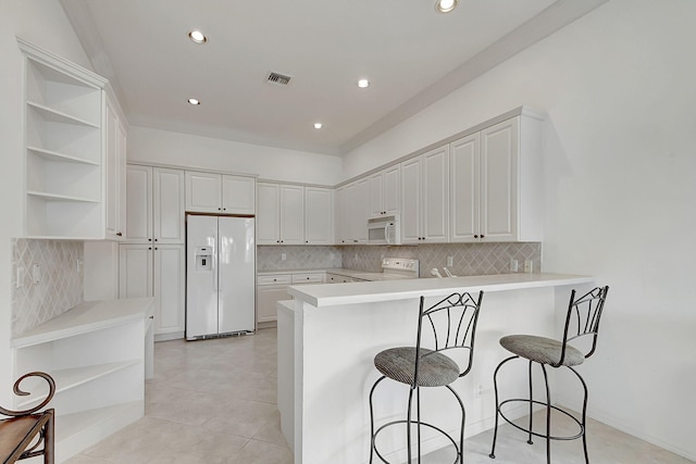 kitchen with a breakfast bar, tasteful backsplash, white cabinetry, light tile floors, and white appliances