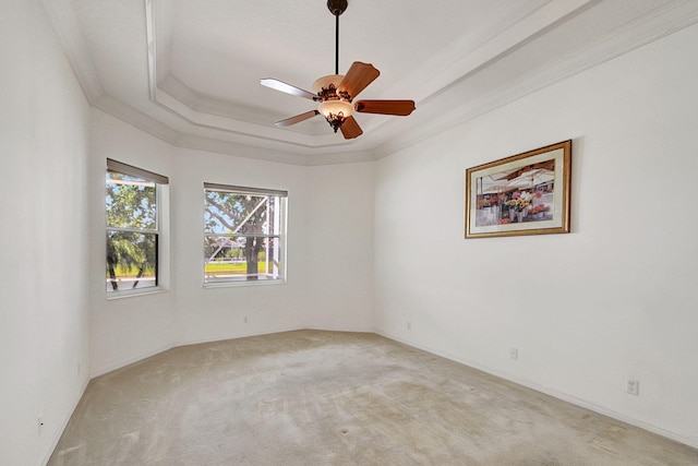 spare room with ceiling fan, ornamental molding, light colored carpet, and a tray ceiling