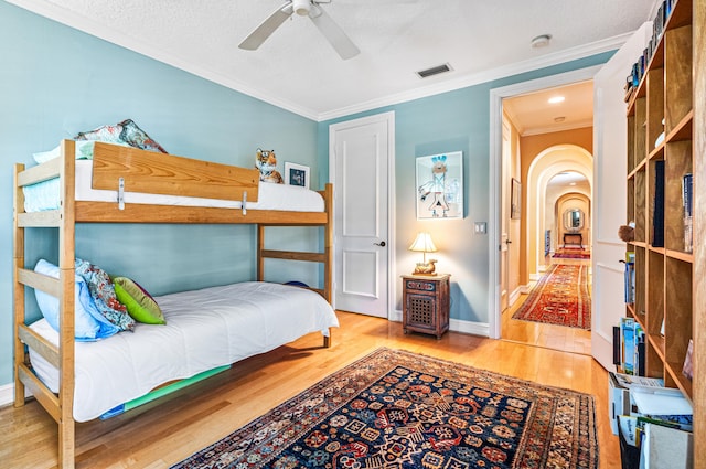 bedroom featuring light hardwood / wood-style flooring, ceiling fan, crown molding, and a textured ceiling