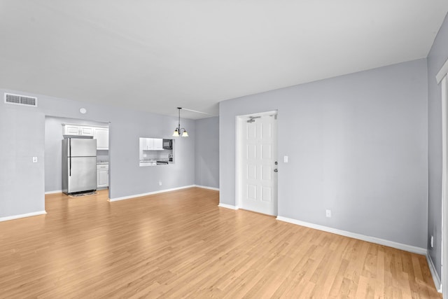 unfurnished living room with light hardwood / wood-style floors and an inviting chandelier