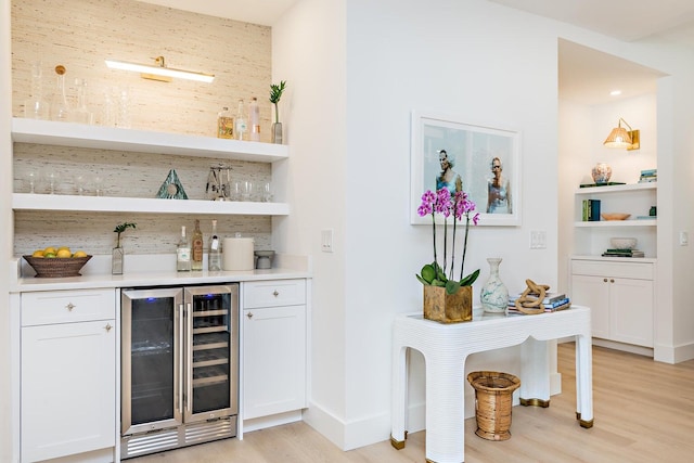 bar with wine cooler, light wood-type flooring, and white cabinets