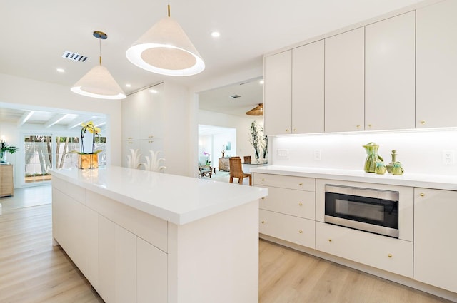 kitchen with beamed ceiling, light hardwood / wood-style floors, white cabinetry, stainless steel microwave, and hanging light fixtures