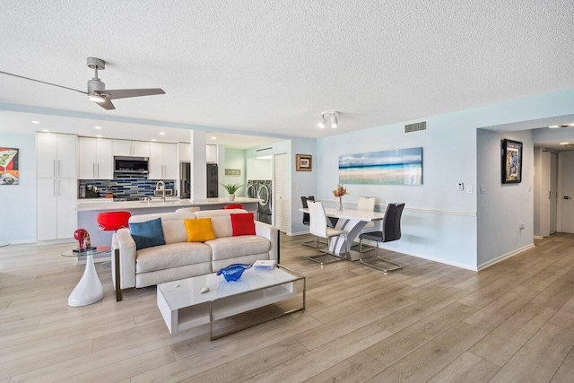 living room featuring sink, light hardwood / wood-style flooring, ceiling fan, and a textured ceiling