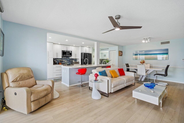 living room featuring sink, light hardwood / wood-style flooring, ceiling fan, and a textured ceiling