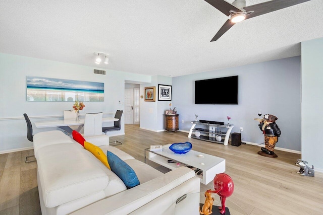 living room featuring light hardwood / wood-style flooring, ceiling fan, and a textured ceiling