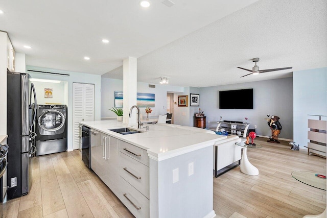 kitchen with sink, light wood-type flooring, white cabinetry, stainless steel fridge, and a center island with sink